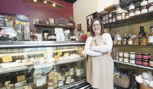 Andrea McEvoy stands in front of a deli case showcasing the cheeses available at Abbie & Oliver’s.