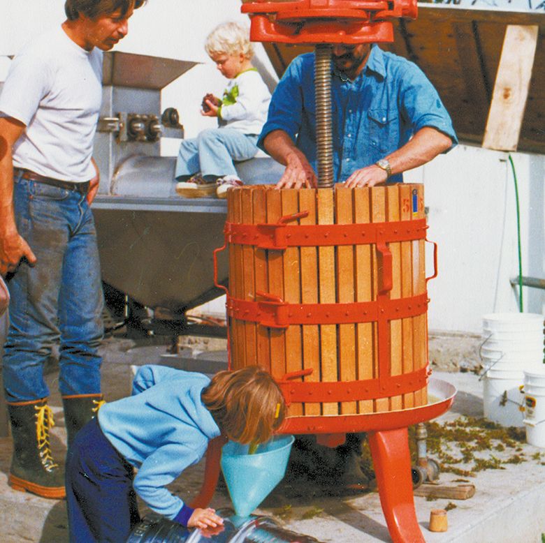 Walla Walla s Figgins family crushing grapes with help from Rick Small of Woodward Canyon. Frm left to right: Gary Figgins, Amy Figgins, Chris Figgins, Rick Small. Taken at Leonetti Cellar, 1976. ##Photo courtesy of Leonetti Cellar