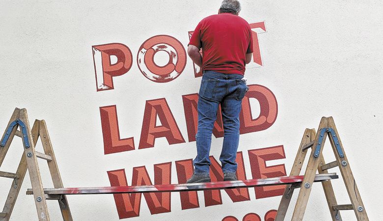 A contractor paints the modern-looking logo on Portland Wine Company’s newly revitalized building in Southeast Portland. ##Photo provided
