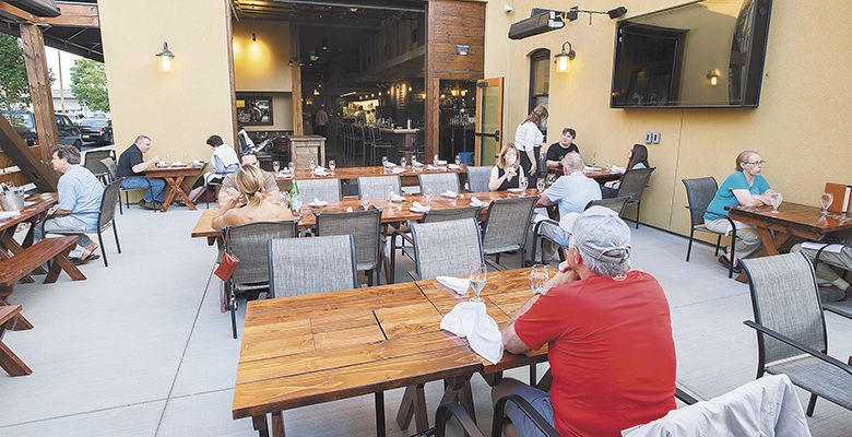 Guests relax on the patio adjacent to the Wine Village, which can be entered via a roll-up door. A massive TV hangs on the wall for special sporting events and overhead heaters for chillier weather.##Photo by Marcus Larson