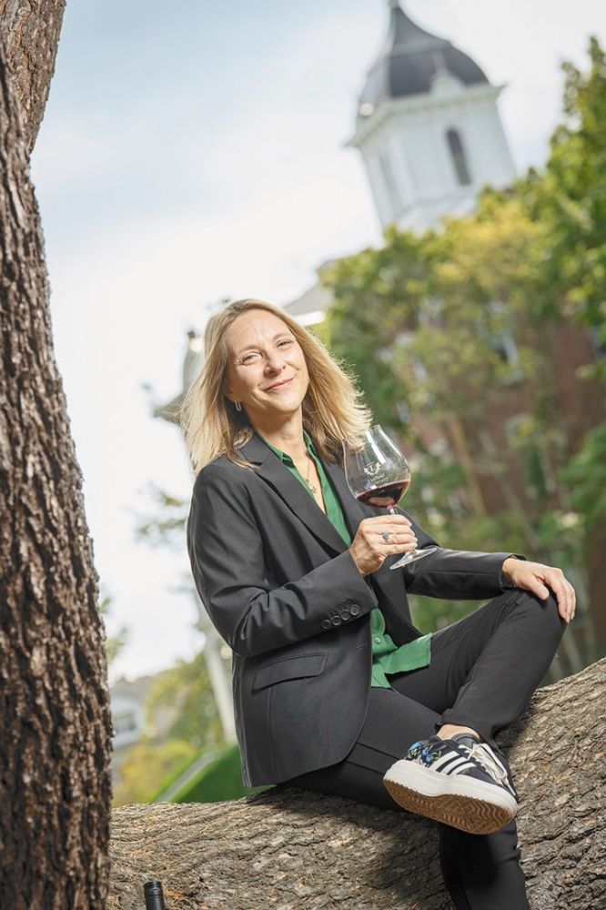 Toni Ketrenos holding a glass of red wine while sitting in a campus tree. ## Photo by F. Miller Photography