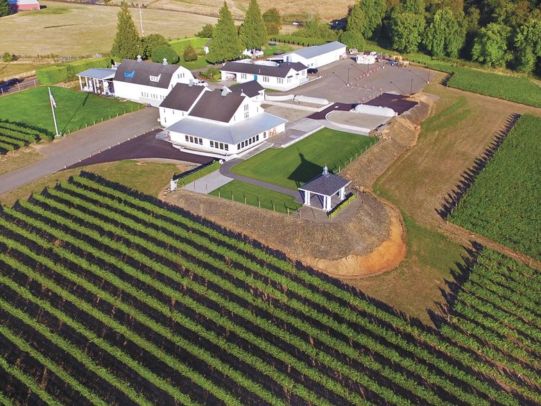 Aerial view of the winery grounds with several restored white barns, surrounded by vineyards.##Photo by Aniko Photography