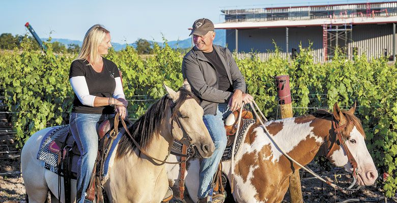 Owners Jen and Ross Allen often ride the vineyard’s perimeter — the new winery is shown under construction in the background. ##Photos © David Gibb Photography | www.dgibbphoto.com