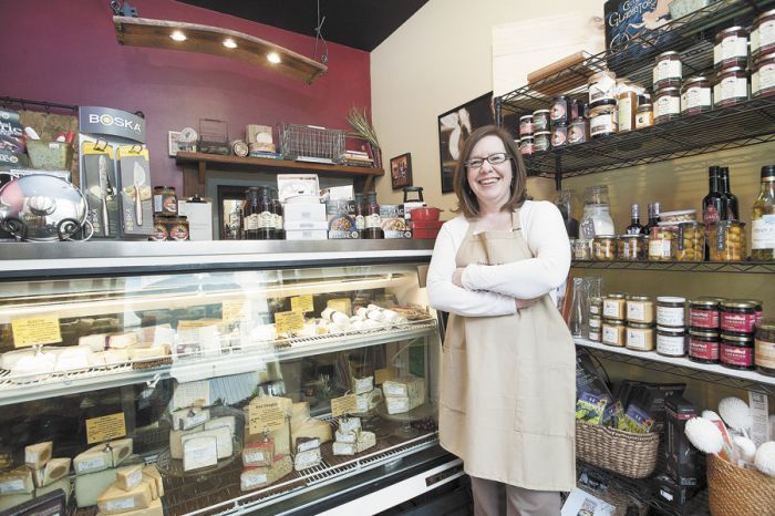 Andrea McEvoy stands in front of a deli case showcasing the cheeses available at Abbie & Oliver’s.