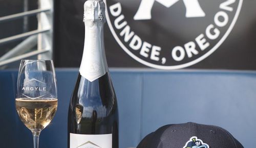 A glass of Argyle Winery sparkling wine, bottle, cap and baseball at the Hillsboro Hops&rsquo; Dugout Lounge. ## Photo provided by Argyle Winery