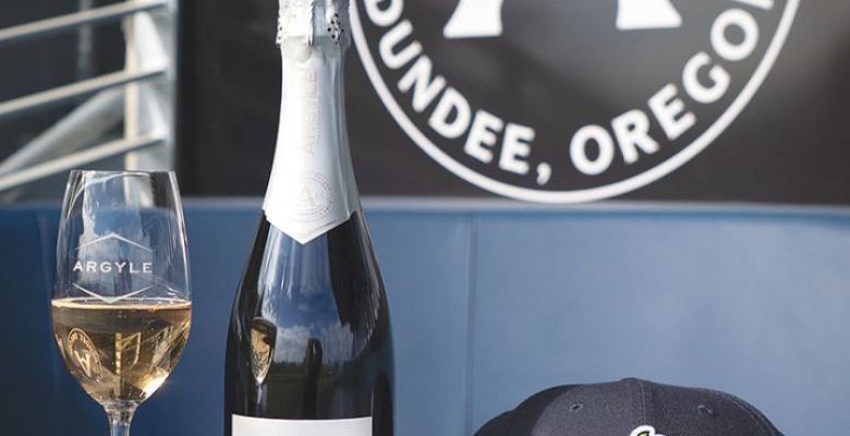 A glass of Argyle Winery sparkling wine, bottle, cap and baseball at the Hillsboro Hops&rsquo; Dugout Lounge. ## Photo provided by Argyle Winery