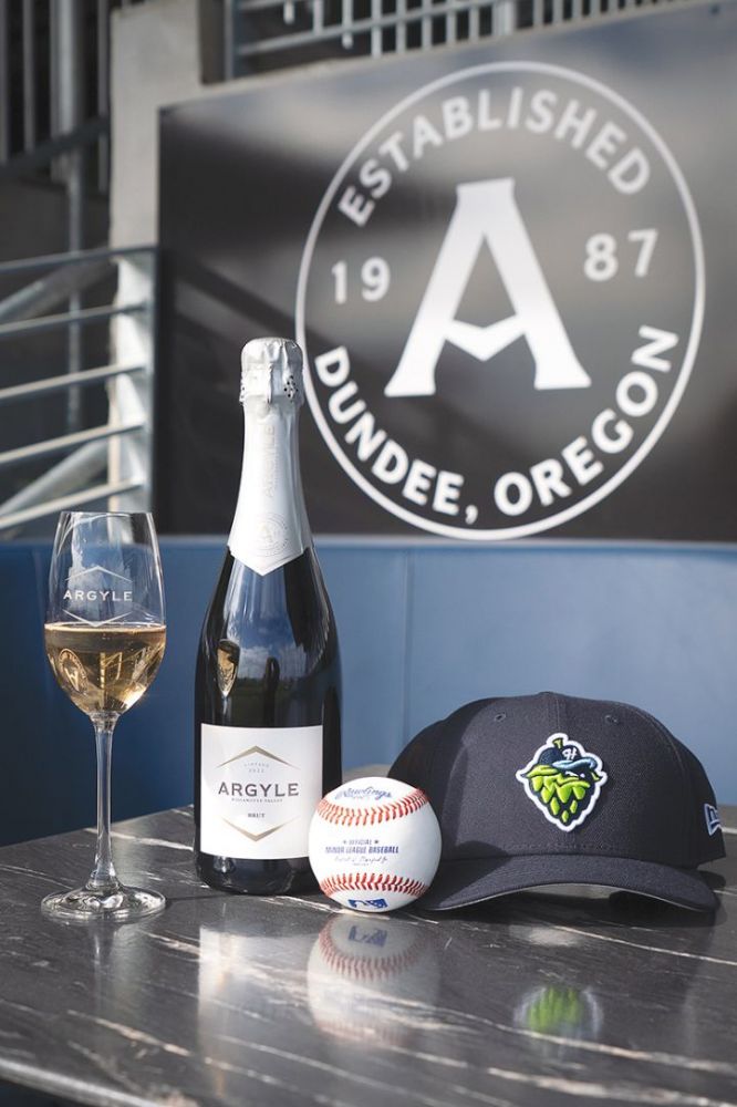 A glass of Argyle Winery sparkling wine, bottle, cap and baseball at the Hillsboro Hops&rsquo; Dugout Lounge. ## Photo provided by Argyle Winery