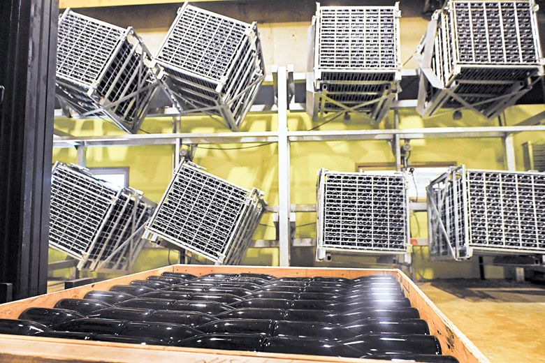 Gyropallet riddling cages filled with bottles hang on the wall as the wine goes through the Méthode Champenoise process. The bottles laying down in the wooden crate are currently being aged.