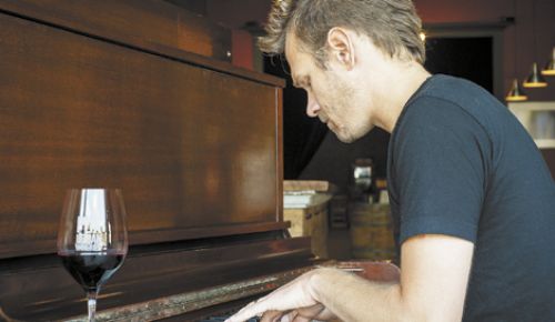 ENSO winemaker/owner Ryan Lee Sharp plays an original song at the winery’s tasting room/lounge. The turn-of-the-century piano belongs to Dave Nicolardi, an ENSO regular, who is scheduled to play at the winery every other Wednesday. Photo by Andrea Johnson.