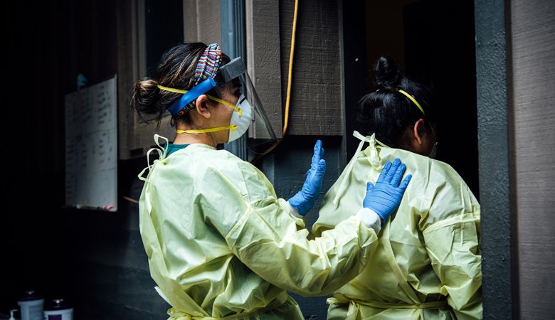 Erika Sanchez Lerma, R.N., outreach nurse, helps Miriam Lopez, program assistant, secure her gown before the vineyard workers arrive for COVID-19 testing at Willakenzie Estate. ##Photo by Kathryn Elsesser