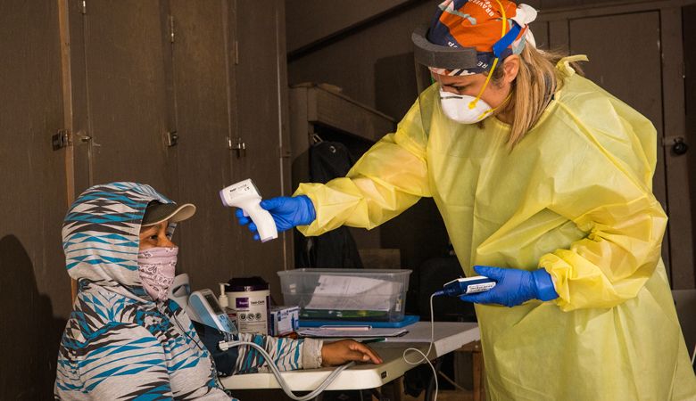 ¡Salud! clinical outreach health educator Andrea Lara Silva, M.P.H., takes the temperature of a clinic attendee using non-contact infrared digital thermometer. ##Photo by Kathryn Elsesser