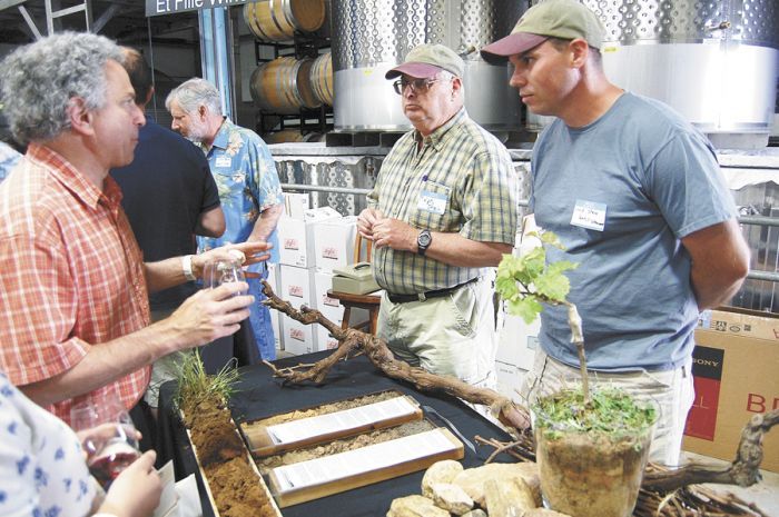 Winegrowers Ralph and Chris Stein, of Yamhill Vineyards, talk terroir with an attendee at the display table featuring soils and an unearthed vine. Photo by Hilary Berg. Winegrowers Ralph and Chris Stein, of Yamhill Vineyards, talk terroir with an attendee at the display table featuring soils and an unearthed vine. Photo by Hilary Berg.