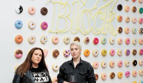 Bree Stock, co-owner of Limited Addition Wines and consulting winemaker for Artist Block (left) with Artist Block founder Anna Sweet. Adorning the wall is Sweet’s whimsical art installation. Each donut is available for purchase. More of Sweet’s art is displayed in the tasting room for guests to enjoy (and buy right off the walls).##Photo by Anna Sweet, owner of Artist Block, assisted by Emma Schmitt