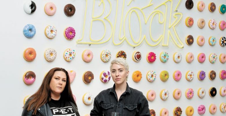 Bree Stock, co-owner of Limited Addition Wines and consulting winemaker for Artist Block (left) with Artist Block founder Anna Sweet. Adorning the wall is Sweet’s whimsical art installation. Each donut is available for purchase. More of Sweet’s art is displayed in the tasting room for guests to enjoy (and buy right off the walls).##Photo by Anna Sweet, owner of Artist Block, assisted by Emma Schmitt