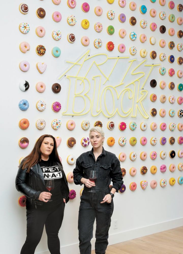 Bree Stock, co-owner of Limited Addition Wines and consulting winemaker for Artist Block (left) with Artist Block founder Anna Sweet. Adorning the wall is Sweet’s whimsical art installation. Each donut is available for purchase. More of Sweet’s art is displayed in the tasting room for guests to enjoy (and buy right off the walls).##Photo by Anna Sweet, owner of Artist Block, assisted by Emma Schmitt