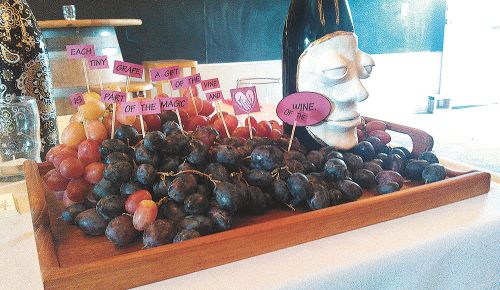 Two artist-decorated bottles stand guard over a tray of tasty grapes at the Drabkin auction. Sequential signs on toothpicks read “Each tiny grape is a gift of the vine and a part of the magic of the wine.” ##Photo provided